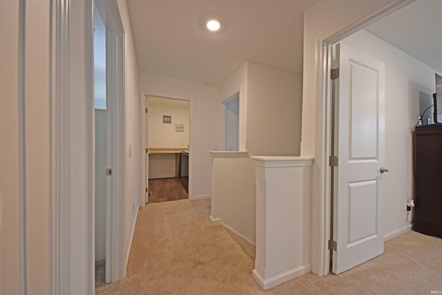 hall featuring an upstairs landing, baseboards, and light colored carpet