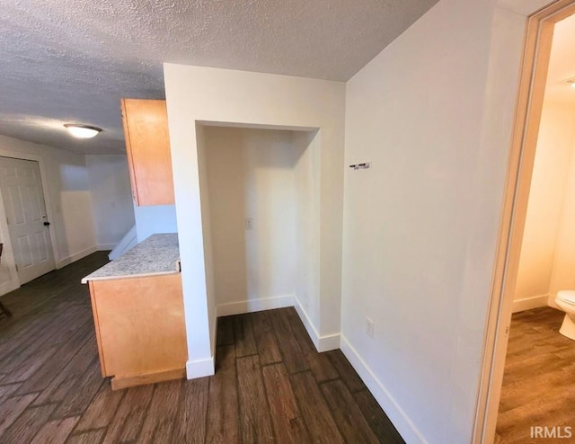 hallway with a textured ceiling, baseboards, and dark wood-type flooring