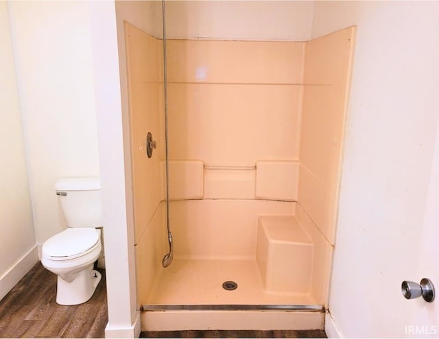 bathroom featuring toilet, a stall shower, baseboards, and wood finished floors