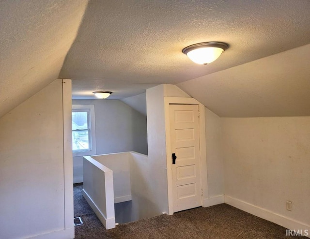 additional living space with dark colored carpet, vaulted ceiling, a textured ceiling, and baseboards