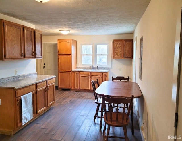 kitchen featuring brown cabinetry, dark wood-style floors, light countertops, a textured ceiling, and a sink