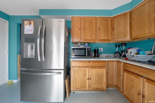 kitchen featuring concrete flooring, brown cabinetry, stainless steel appliances, and light countertops