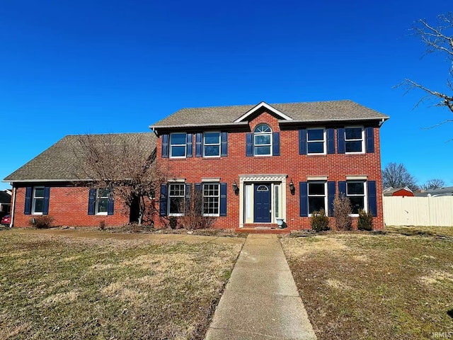 colonial inspired home featuring brick siding, fence, and a front lawn