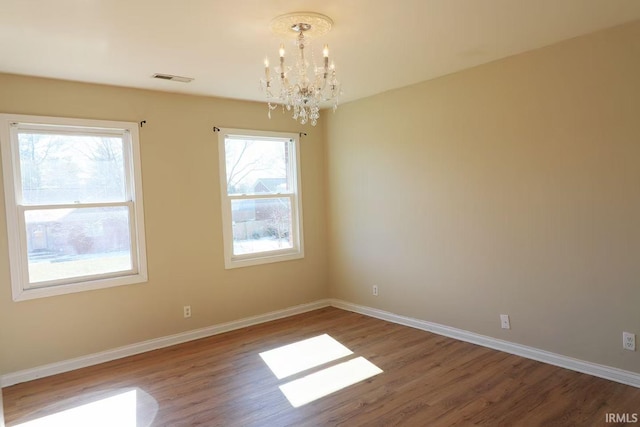 spare room with an inviting chandelier, wood finished floors, visible vents, and baseboards