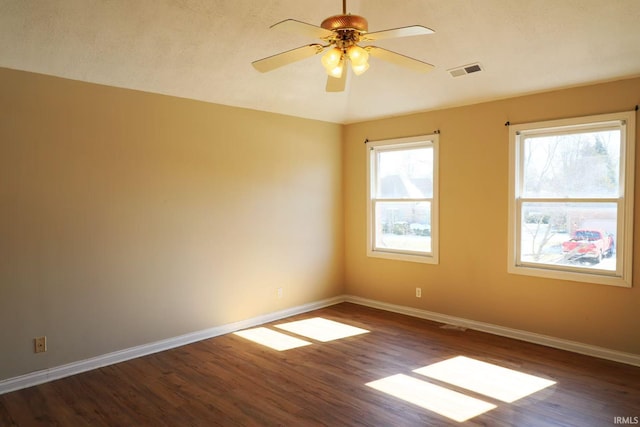 spare room featuring baseboards, visible vents, ceiling fan, and dark wood-style flooring