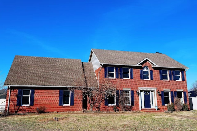 colonial inspired home with brick siding, a front yard, and a shingled roof