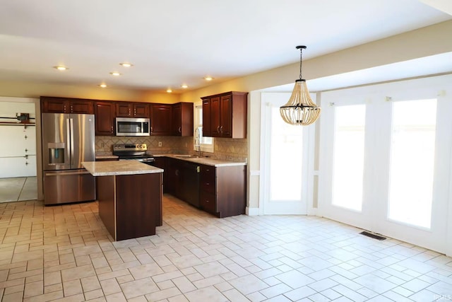 kitchen with visible vents, a kitchen island, appliances with stainless steel finishes, decorative light fixtures, and backsplash