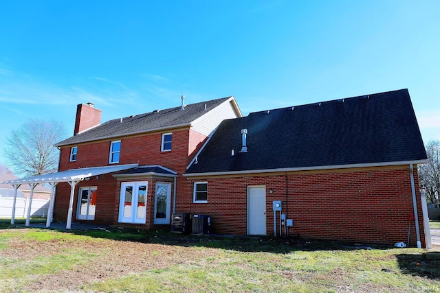 back of property featuring a yard, french doors, brick siding, and a chimney