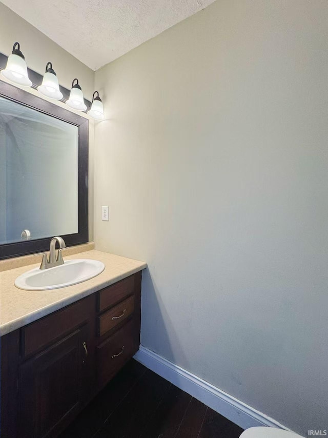 bathroom featuring baseboards, wood finished floors, a textured ceiling, and vanity