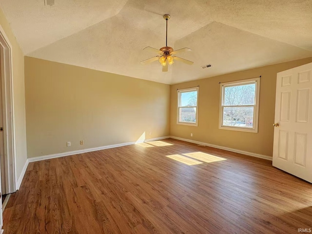 spare room with baseboards, visible vents, ceiling fan, wood finished floors, and vaulted ceiling