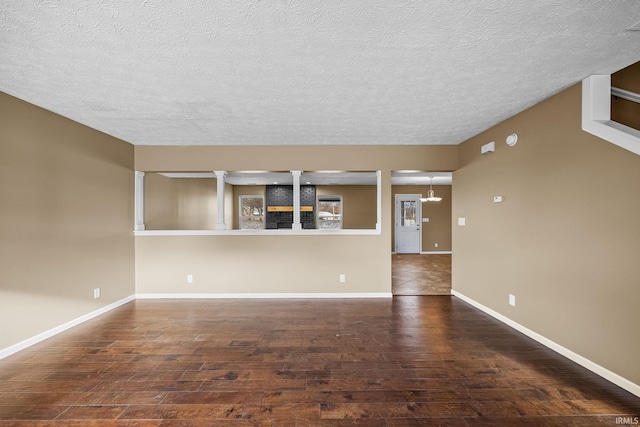 unfurnished living room featuring ornate columns, baseboards, and wood finished floors