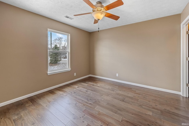 spare room featuring visible vents, ceiling fan, baseboards, and wood finished floors