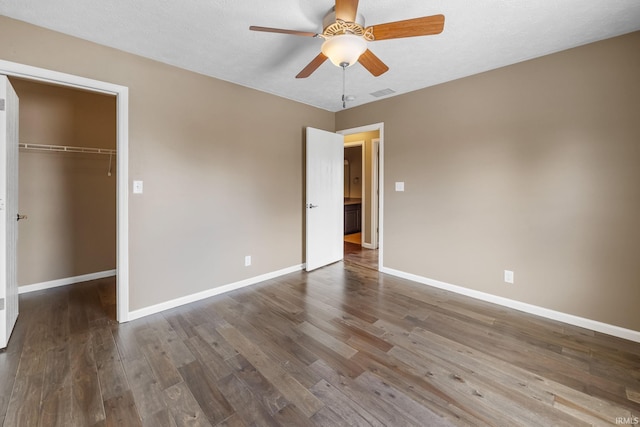 unfurnished bedroom with a walk in closet, a closet, visible vents, wood finished floors, and baseboards