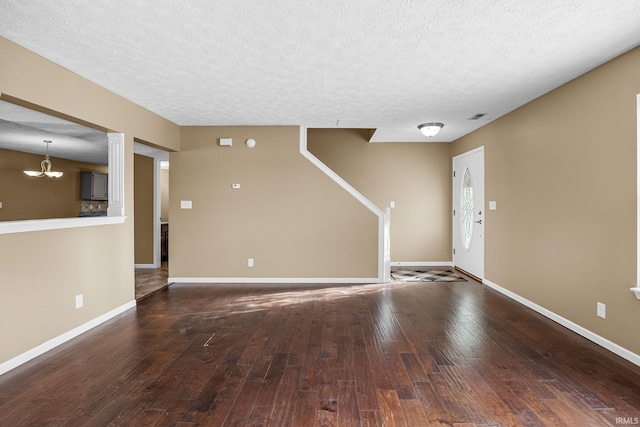 unfurnished living room with an inviting chandelier, a textured ceiling, baseboards, and hardwood / wood-style flooring