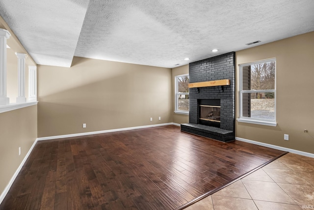 unfurnished living room featuring a brick fireplace, baseboards, visible vents, and wood finished floors