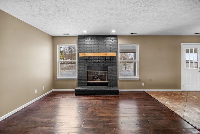 unfurnished living room with a fireplace, wood finished floors, visible vents, and baseboards