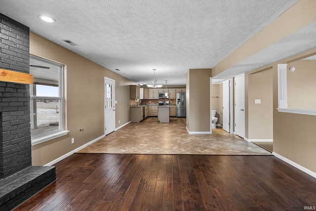 unfurnished living room with light wood-style floors, baseboards, visible vents, and a textured ceiling