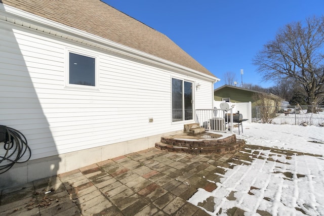 snow covered house with a shingled roof, fence, central AC, and a patio