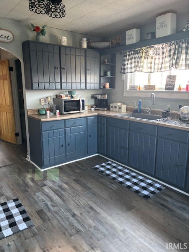 kitchen with arched walkways, stainless steel microwave, dark wood-style flooring, blue cabinets, and a sink