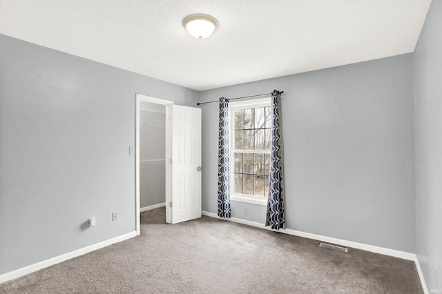 carpeted spare room with a textured ceiling, visible vents, and baseboards