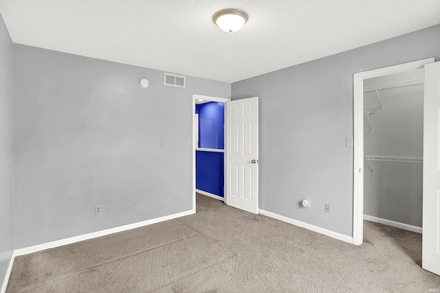 unfurnished bedroom with carpet, visible vents, and a walk in closet