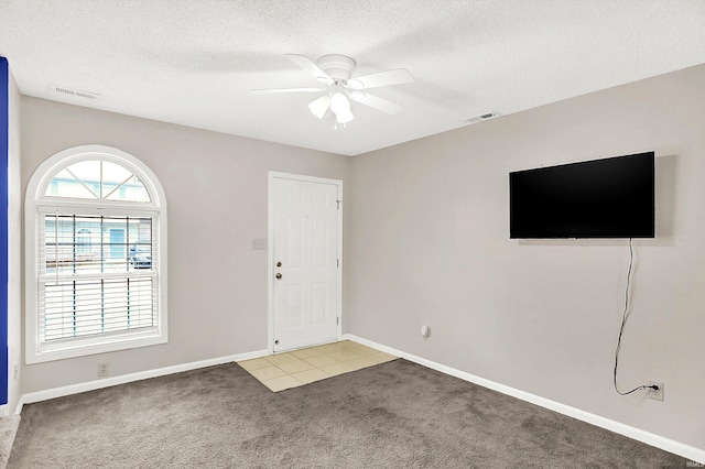 foyer featuring visible vents, ceiling fan, light carpet, and a textured ceiling