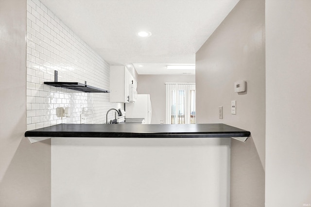 kitchen with open shelves, backsplash, freestanding refrigerator, a sink, and a peninsula