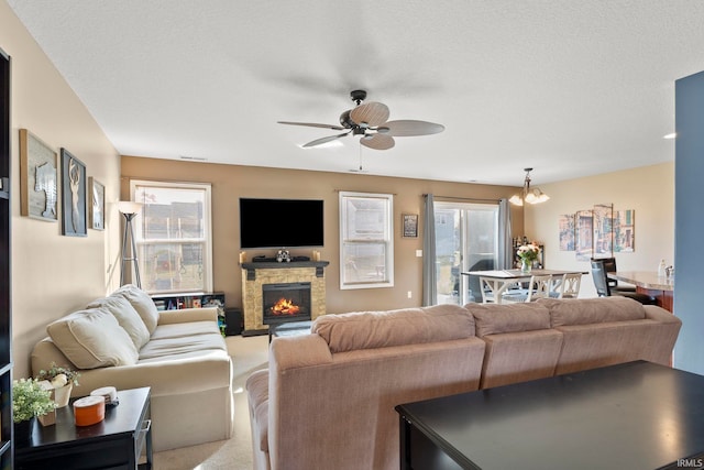 carpeted living area featuring a ceiling fan, a stone fireplace, and a textured ceiling