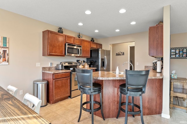 kitchen with a breakfast bar area, a peninsula, stainless steel appliances, light countertops, and a sink