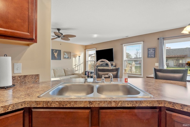 kitchen featuring ceiling fan, a sink, open floor plan, light countertops, and brown cabinetry