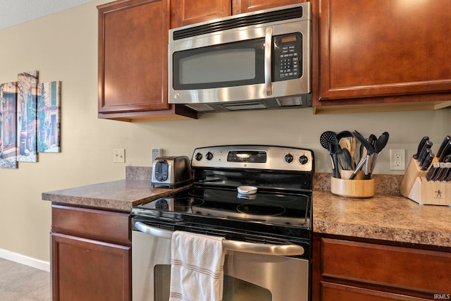 kitchen featuring stainless steel appliances, brown cabinetry, and baseboards