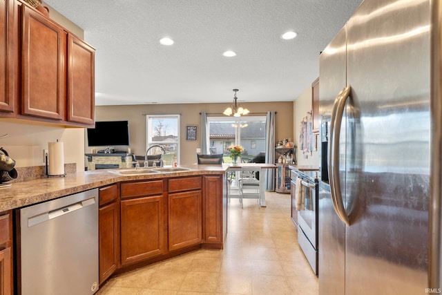 kitchen with a textured ceiling, a peninsula, a sink, appliances with stainless steel finishes, and brown cabinets