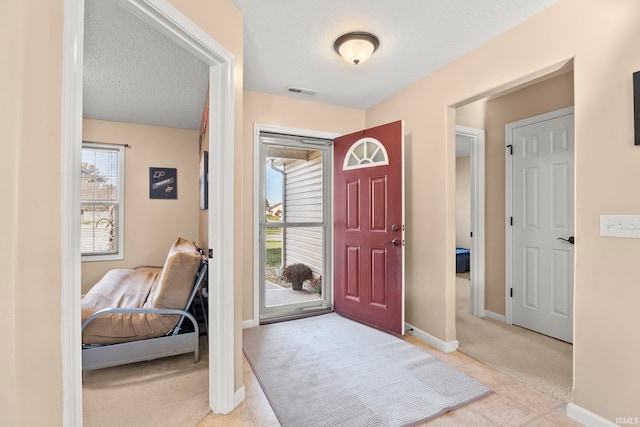 entryway with light tile patterned floors, visible vents, light carpet, a textured ceiling, and baseboards