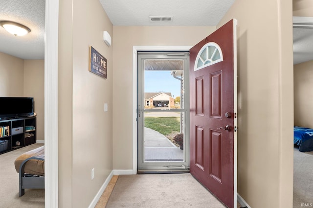 entrance foyer featuring a textured ceiling, carpet flooring, visible vents, and baseboards