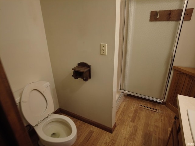 bathroom featuring toilet, a shower stall, baseboards, and wood finished floors