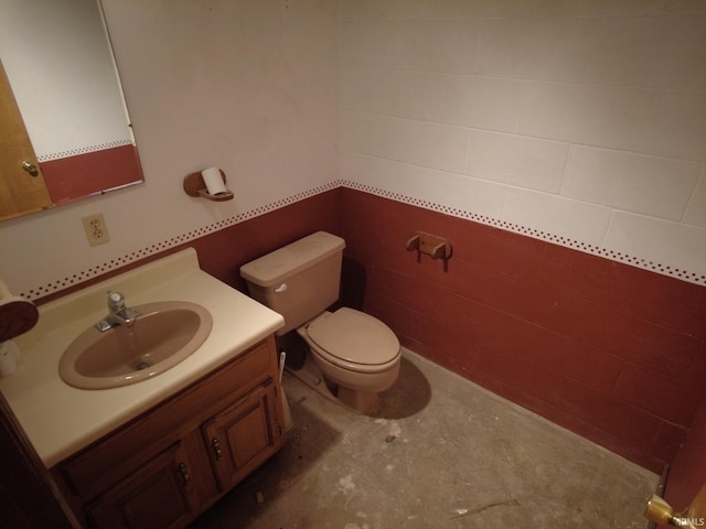 half bathroom with toilet, concrete block wall, vanity, and concrete flooring