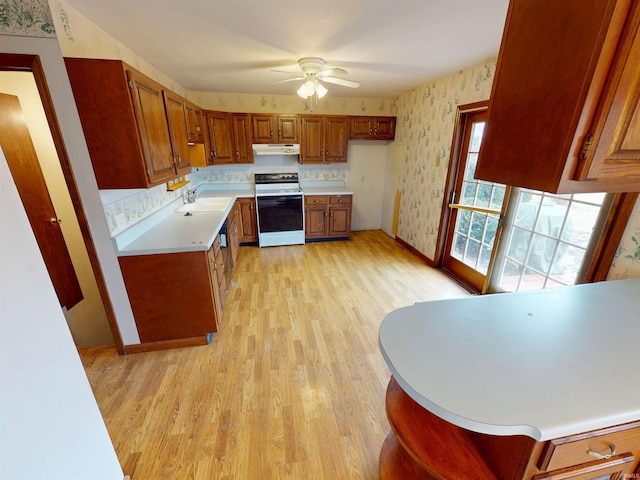 kitchen featuring light countertops, electric range, brown cabinetry, under cabinet range hood, and wallpapered walls