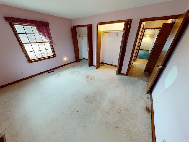 unfurnished bedroom featuring light colored carpet, visible vents, baseboards, and two closets