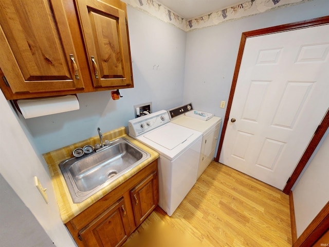 laundry room featuring washing machine and dryer, cabinet space, a sink, and light wood finished floors