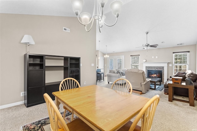 dining space featuring light carpet, ceiling fan with notable chandelier, visible vents, baseboards, and a glass covered fireplace