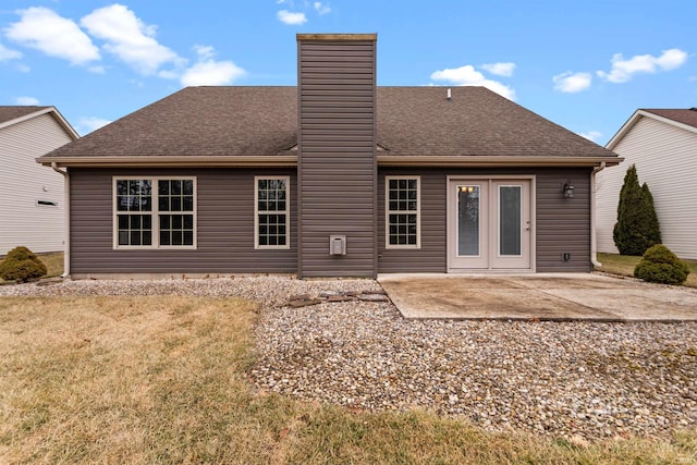 rear view of property with roof with shingles, a chimney, a patio area, and a lawn