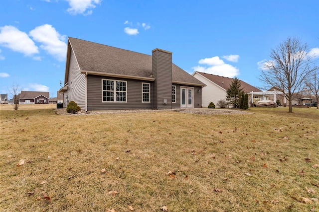 rear view of property featuring roof with shingles, a chimney, and a yard