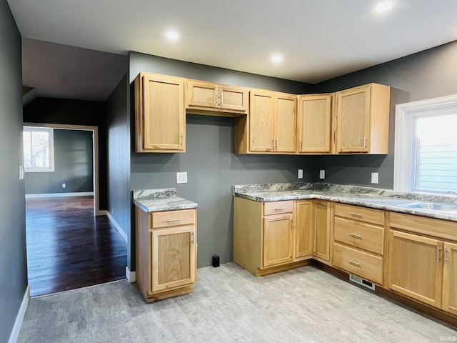 kitchen featuring light countertops, light brown cabinetry, a sink, light wood-type flooring, and baseboards