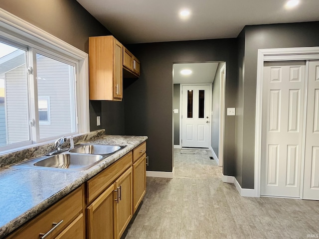 kitchen with light wood-style flooring, baseboards, brown cabinets, and a sink