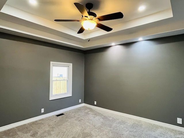 empty room with ceiling fan, carpet floors, visible vents, baseboards, and a tray ceiling