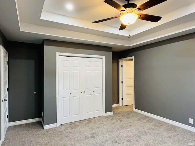 unfurnished bedroom with a closet, a raised ceiling, light colored carpet, and baseboards