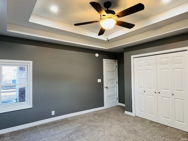 unfurnished bedroom featuring ceiling fan, light carpet, baseboards, a closet, and a raised ceiling