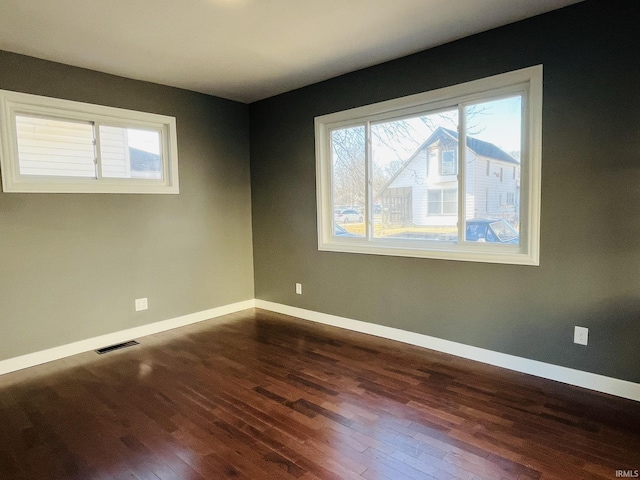 empty room with dark wood-style floors, visible vents, and baseboards