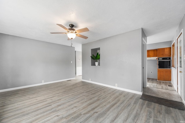 spare room featuring light wood-type flooring, ceiling fan, baseboards, and a textured ceiling