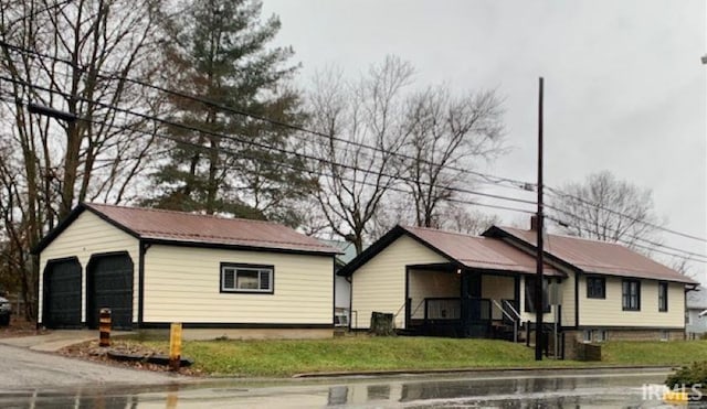 single story home featuring an outbuilding, covered porch, metal roof, a front yard, and a garage